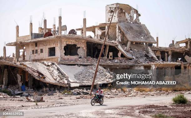 Syrian rides a motorcycle past destroyed buildings in an opposition-held neighbourhood of the southern city of Daraa on October 2, 2018.