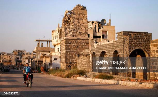 Syrian man rides a motorcycle while carrying a gas cylinder as he drives past the Omari mosque in a rebel-held area in the southern Syrian city of...