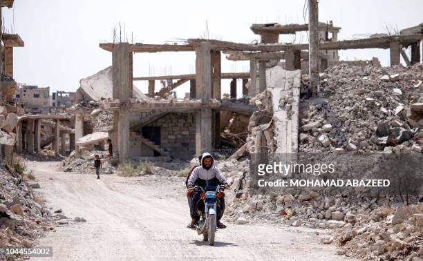 Syrians ride a bicycle past destroyed buildings in an opposition-held neighbourhood of the southern city of Daraa on October 2, 2018.