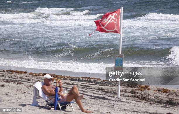 Richard Desmoni of Boca Raton, Fla. Rests near a red flag warning people of severe hazards in the water at Red Reef Park in Boca Raton on Tuesday,...