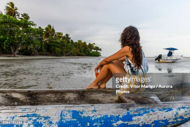 photograph of young woman sitting in wooden canoe by tropical beach, boipeba island, south bahia, brazil - wavy hair beach stock pictures, royalty-free photos & images