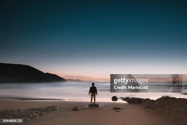 silhouette of young man at empty beach at night - praia noite imagens e fotografias de stock