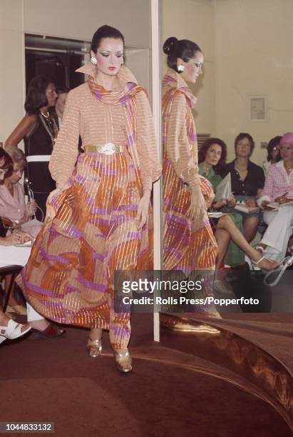 View of a young female fashion model wearing a swirling chiffon evening skirt in pink and peach combined with gold stripes worn with a blouse...