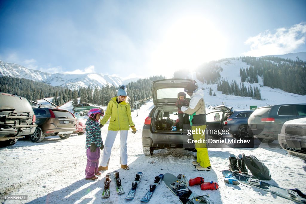 Mixed race family at a parking lot unloading ski and snowboard equipment out of their car and getting the kids ready for a day on the mountain.
