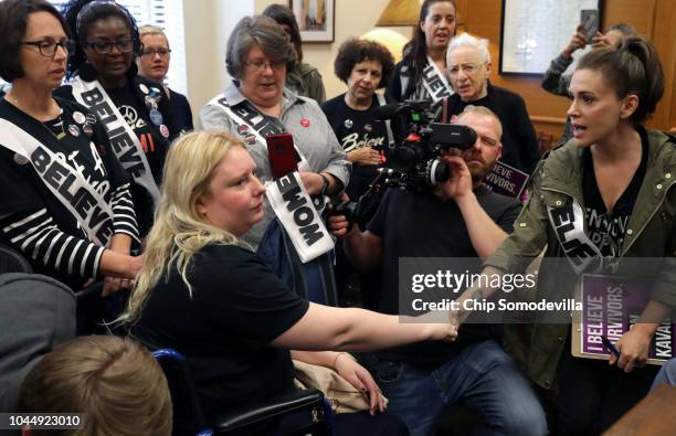 Actor Alyssa Milano holds hands with Emily Thompson as she recounts her story of being sexually assaulted as they and dozens of other protesters...