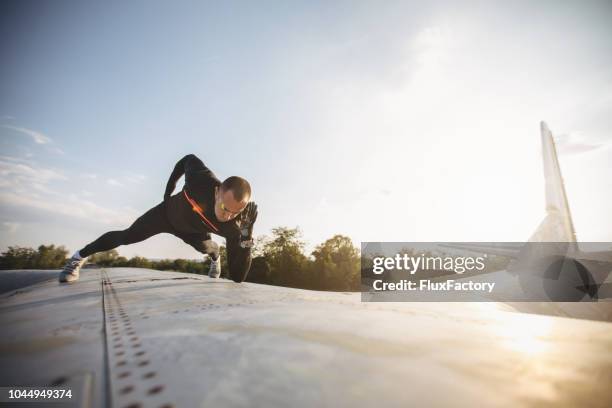 strong and handsome athlete doing a one hand plank on a airplane - daredevils and stunts imagens e fotografias de stock