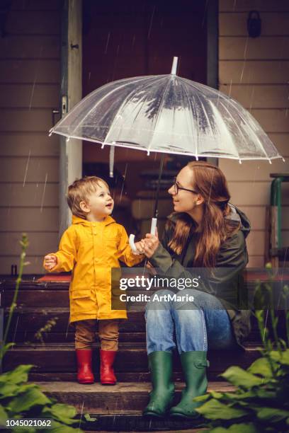 moeder en zoon in regenjassen wandelen in de regen - child umbrella stockfoto's en -beelden