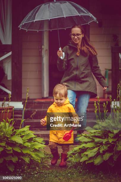 moeder en zoon in regenjassen wandelen in de regen - mother son shower stockfoto's en -beelden
