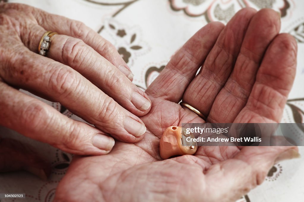 Elderly woman's hands holding a modern hearing aid