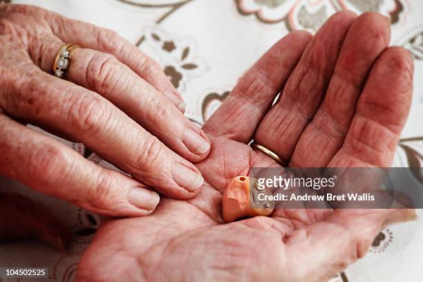 elderly woman's hands holding a modern hearing aid - hearing aids stock pictures, royalty-free photos & images