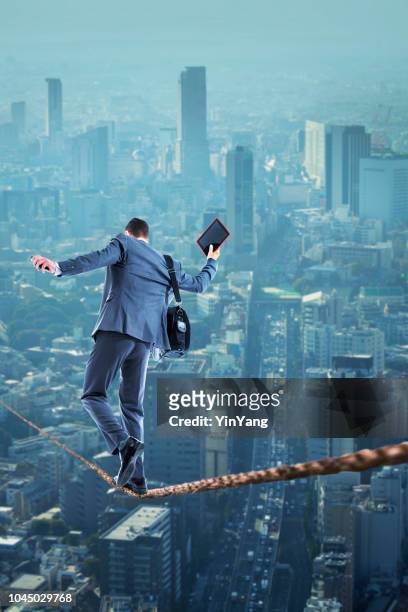businessman walking on tight rope high above the city below - tightrope stock pictures, royalty-free photos & images