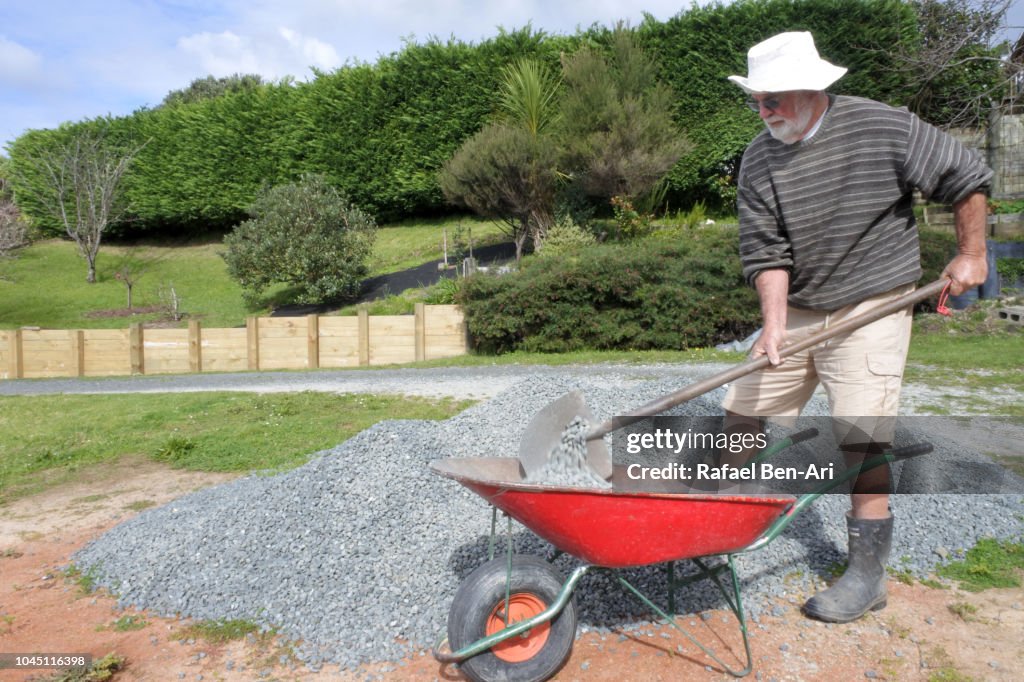 Adult Senior Man Filling a Wheel Barrel with Gravel