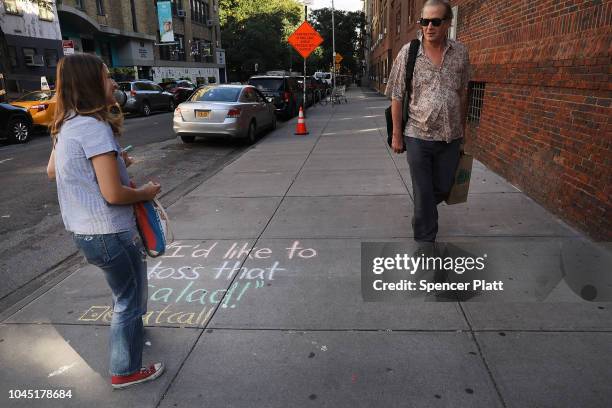 Sophie Sandberg talks to a man as she uses colored chalk to draw a quote on the sidewalk from a catcall made towards a woman on October 3, 2018 in...