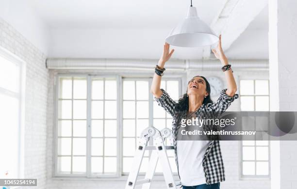 woman hanging a lamp in new home property services. new home. - decoration stock pictures, royalty-free photos & images