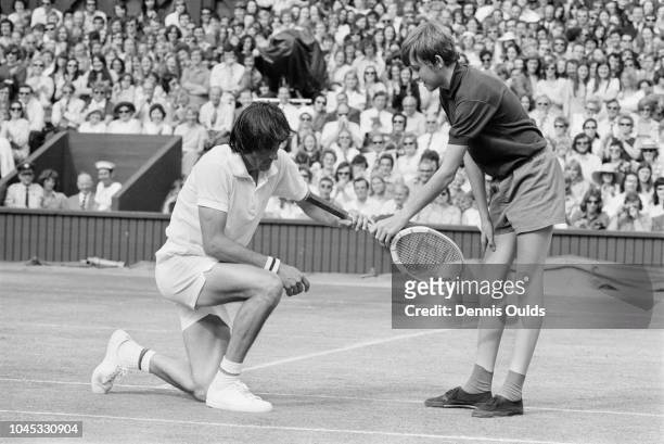 Ball-boy hands back Ilie Nastase's racket after the Romanian tennis player took a fall during his Men's Singles semi-final match against Manuel...