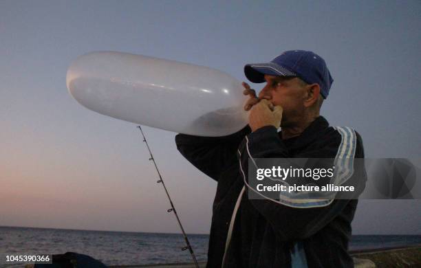 September 2018, Cuba, La Habana: A pescador infla un preservativo para usarlo de flotador del anelo. Todas las tardes cuando empieza a caer el sol...