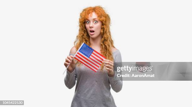 Young redhead woman holding flag of United States of America scared in shock with a surprise face, afraid and excited with fear expression