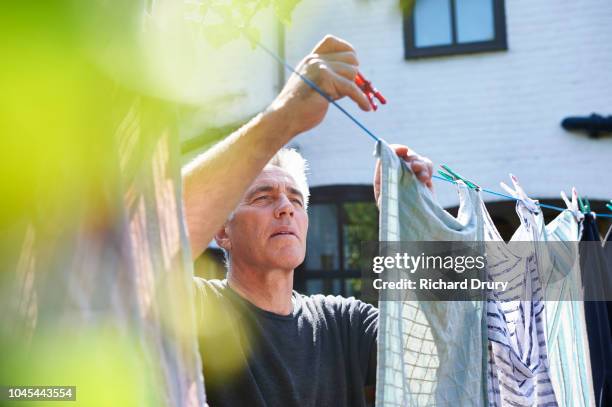 mature man hanging out the washing on the washing line - clothesline stockfoto's en -beelden