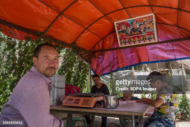 Camel farmers seen waiting for costumers to buy their milk under a shelter with a poster of Chinese leaders hanging there in the Kashgar old Town,...