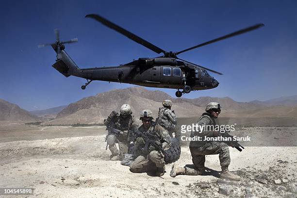 Soldiers from 3rd Brigade, 10th Mountain Division take cover as a UH-60 Blackhawk helicopter takes off after dropping off a replacement tire for a...