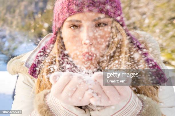 junge frau bläst schnee aus ihren händen - face snow stock-fotos und bilder