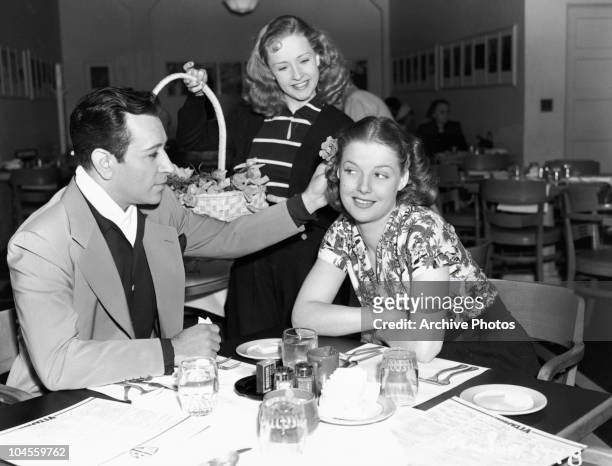 American actor George Raft presents actress Ann Sheridan with a flower provided by actress Bonita Granville in a canteen at Warner Bros Studios,...