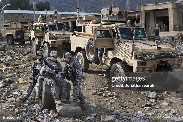 Soldiers from the 4-320th Field Artillery Battalion of the 101st Airborne Division consult a map outside of their MRAP vehicles while escorting a...