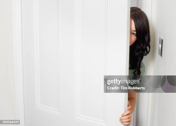 young woman peering out from behind door. - woman opening door stock pictures, royalty-free photos & images