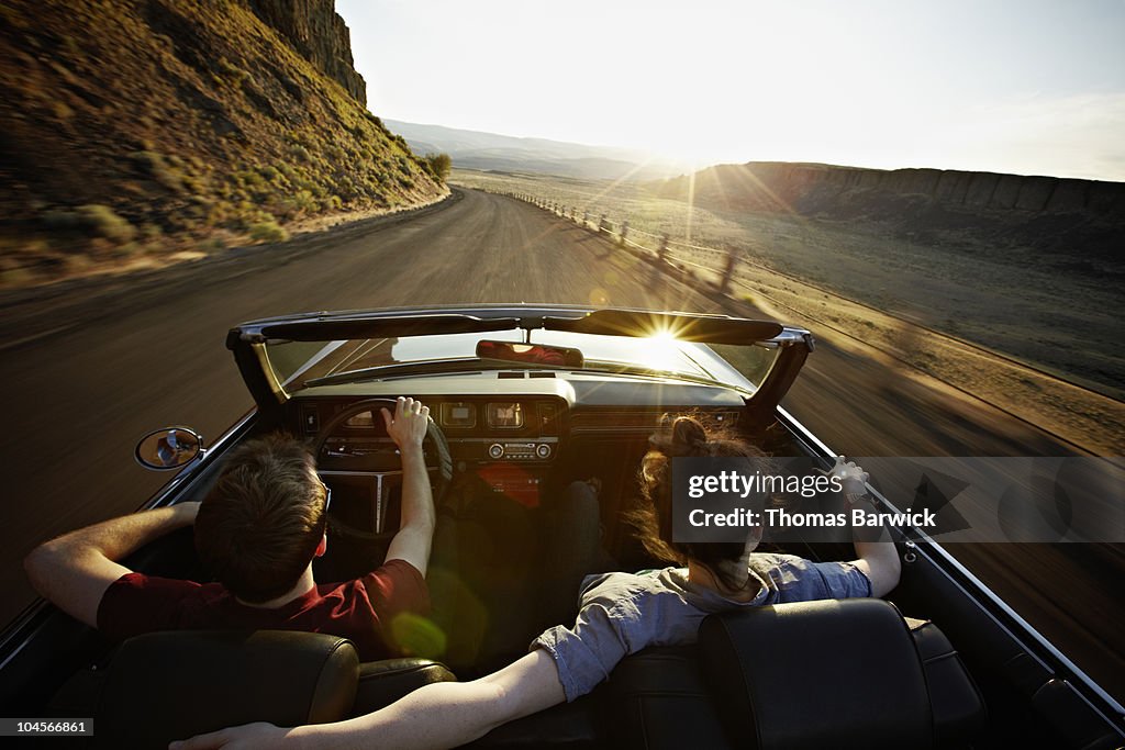 Young couple driving convertible at sunset