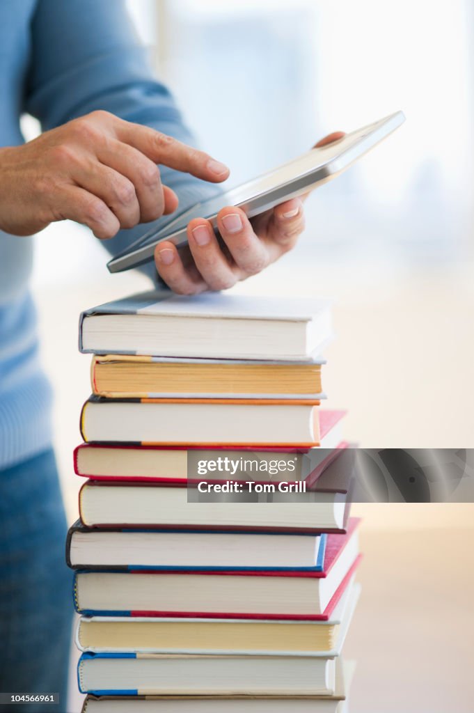 Hand holding digital tablet over stack of books