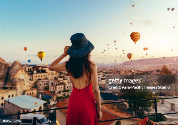 beautiful asian woman watching colorful hot air balloons flying over the valley at cappadocia, turkey. turkey cappadocia fairytale scenery of mountains. - capadócia imagens e fotografias de stock