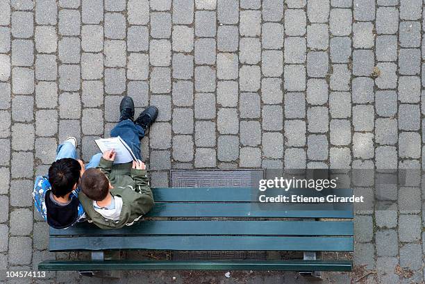 two boys sitting on a park bench looking at a book - banc photos et images de collection