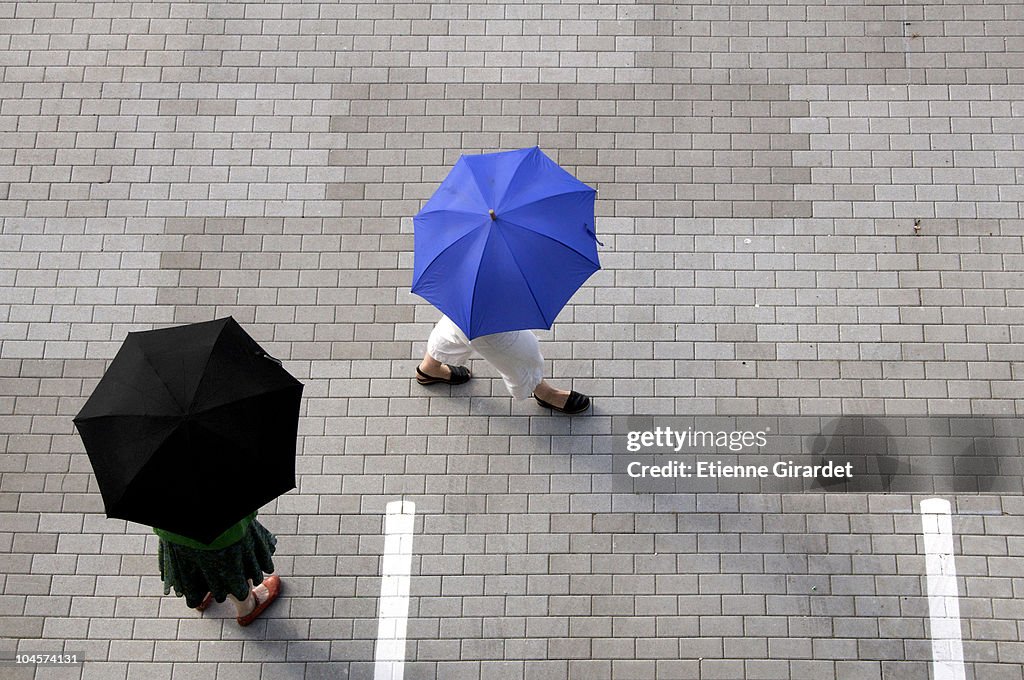 Two women with umbrellas walking through a parking lot