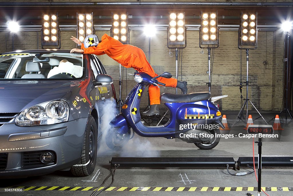 A crash test dummy on a scooter crashing into a car