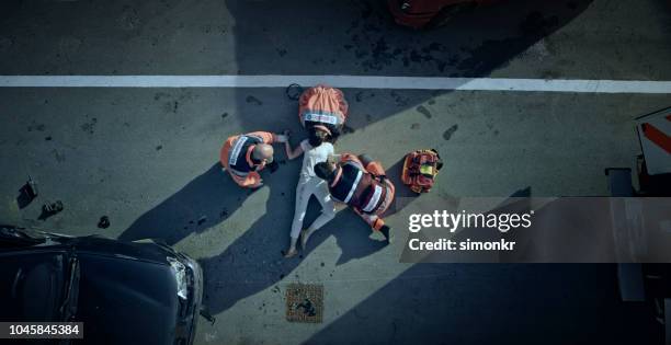 paramedic team checking vital signs of car accident victim lying on ground at car crash site - disaster victim stock pictures, royalty-free photos & images