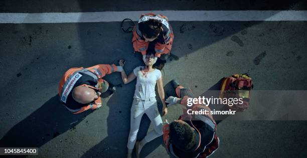 paramedic team checking vital signs of car accident victim lying on ground at car crash site - disaster victim stock pictures, royalty-free photos & images