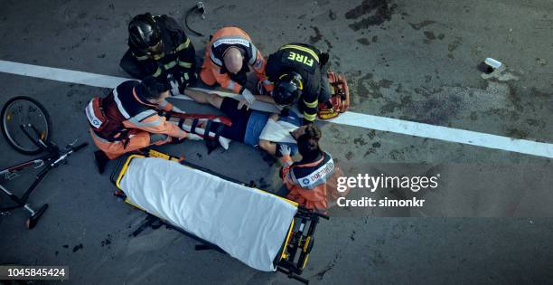 paramedici en brandweerlui verhogen van een gewonde man fietser op de brancard op plaats van ongeval - injured street stockfoto's en -beelden