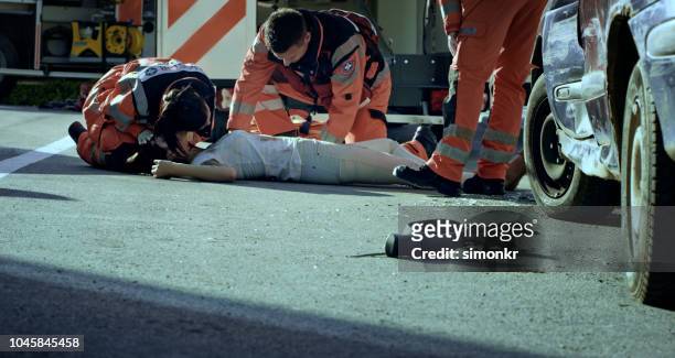 paramedic team checking vital signs of car accident victim lying on ground at car crash site - male victim stock pictures, royalty-free photos & images