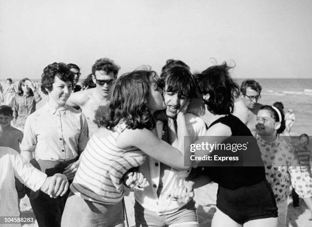 Drummer Ringo Starr of The Beatles on a beach in Miami, Florida, getting kissed by female fans, circa February 1964.