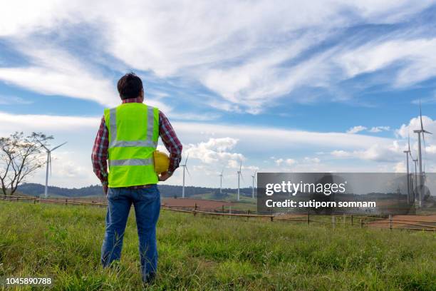 engineering man standing holding helmet looking wind turbines - architect in landscape stock pictures, royalty-free photos & images