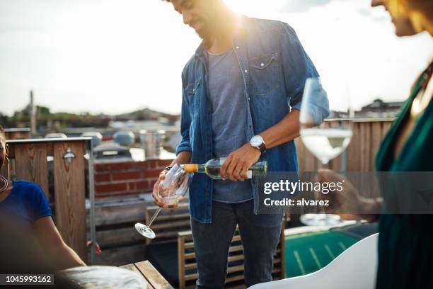 young african man serving wine to friends at rooftop party - champagne rooftop stock pictures, royalty-free photos & images