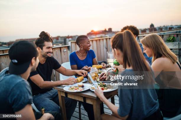 amigos tener comida en la fiesta en la azotea - barbacoa amigos fotografías e imágenes de stock