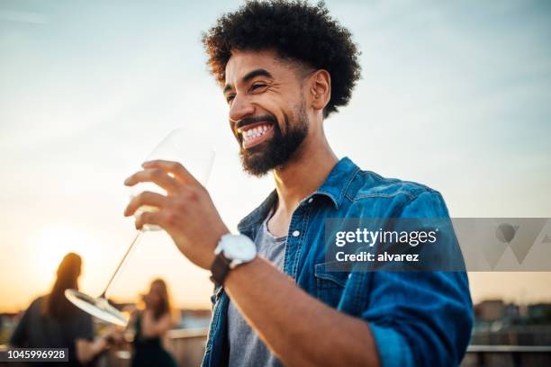 giovane che beve qualcosa alla festa sul tetto al tramonto - men drinking wine foto e immagini stock