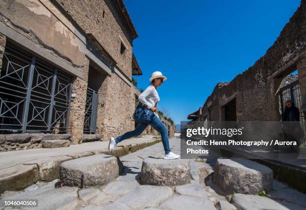female tourist jumping on stones in ruins of pompeii, naples, italy - pompeya fotografías e imágenes de stock