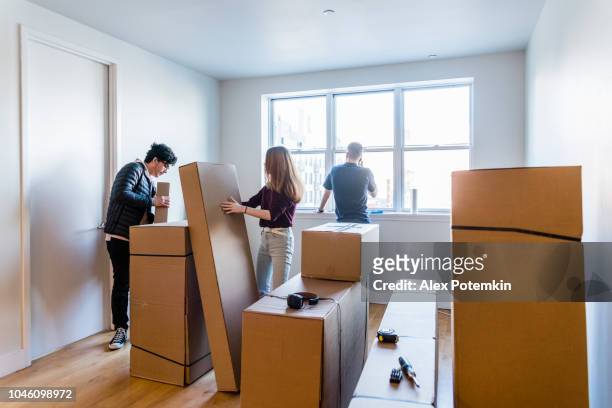 young hispanic latino man helpt zijn vriendin, tiener meisje, kartonnen verhuisdozen met hun spullen in het nieuwe huis wanneer de volwassen man, vader, praten door op te staan van de telefoon in de buurt van bij het raam. - alex boys stockfoto's en -beelden