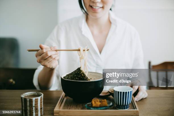 close up shot of smiling young woman enjoying japanese udon soup noodles with side dishes and green tea in restaurant - udon noodle stock pictures, royalty-free photos & images