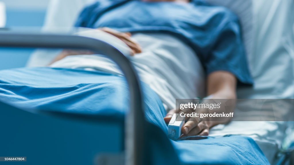 In the Hospital Sick Male Patient Sleeps on the Bed. Heart Rate Monitor Equipment is on His Finger.