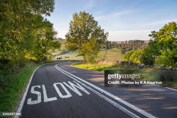 slow sign on sharp bend of a country road - langzaam stockfoto's en -beelden