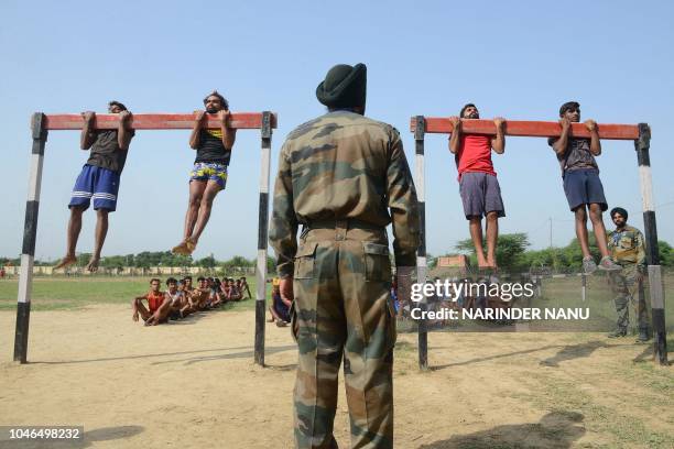 Indian army officer watches candidates performing pull-ups during a physical fitness test at an Indian Army recruitment rally at Khasa, some 15 Km...