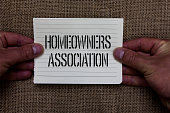Text sign showing Homeowners Association. Conceptual photo Organization with fee for upkeeps of Gated Community Man holding piece notebook paper jute background Communicating ideas.